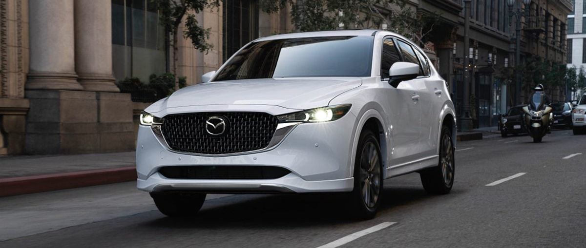 A white 2025 Mazda CX-5 driving on a city street